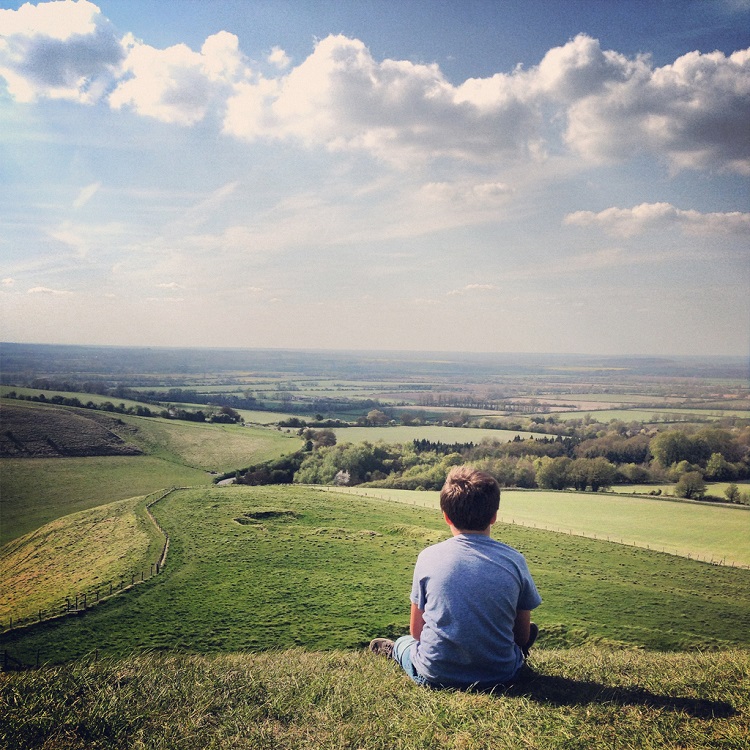 Boy sitting on the hill at White Horse Uffington, seeming lost in thought.